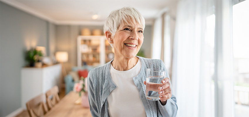 Senior woman smiling while holding a glass of water.